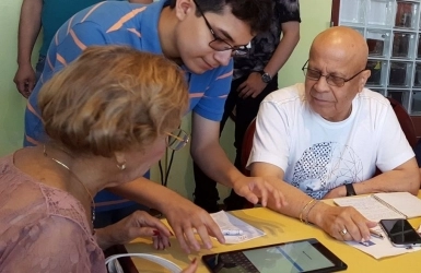 A teen speaking sharing a tablet device with two older adults at a table
